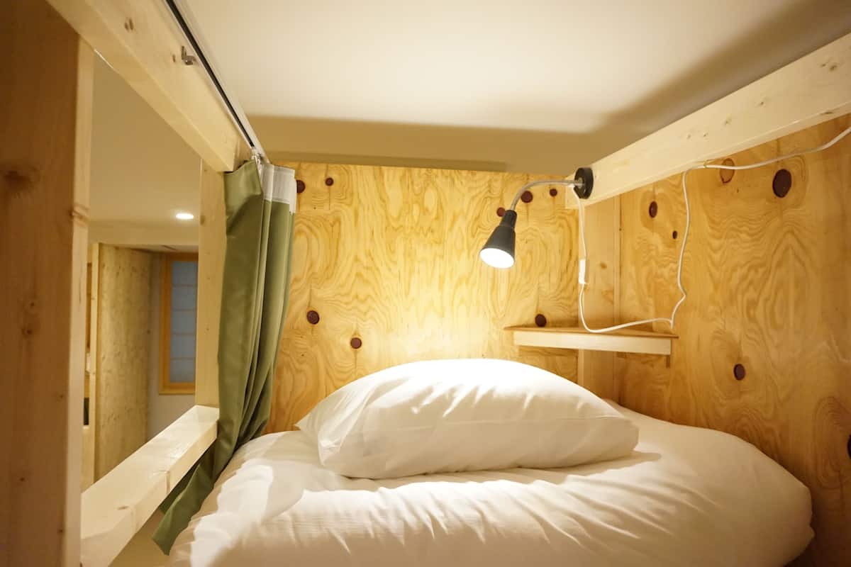 A small, cozy room with a single bed, a green curtain, a wooden headboard, and a wall-mounted shelf.