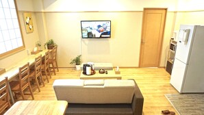 Un espace de vie compact comprenant un canapé, une table à manger, des chaises, un téléviseur et un réfrigérateur.