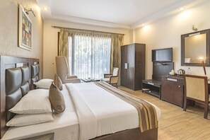 A hotel room with a large bed, a desk, a television, and a wardrobe. - Royal Residence On MG Road (Gurugram)