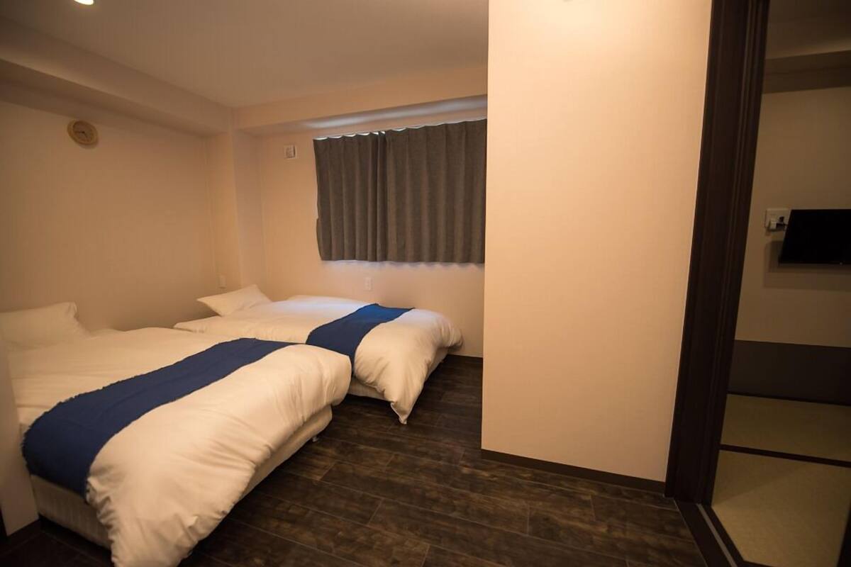 Habitación de hotel con dos camas, una ventana con cortinas y un televisor de pantalla plana montado en la pared.