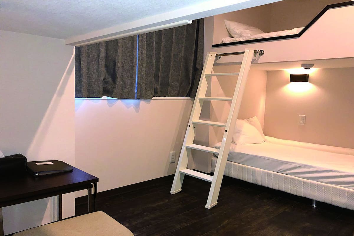 Una habitación pequeña con literas, un escritorio y una escalera.