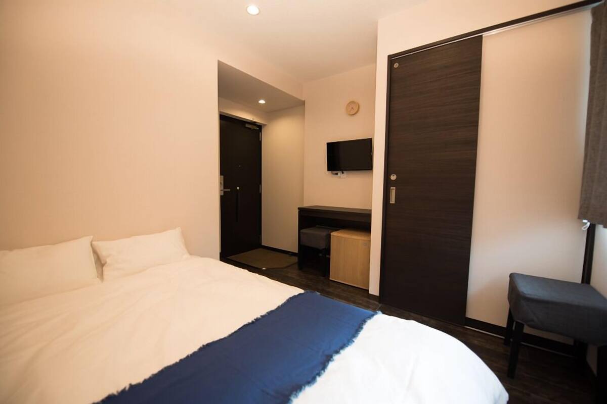 Habitación de hotel con cama, escritorio, silla, televisor y armario.