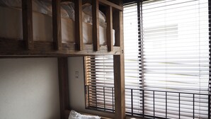 A bunk bed with a wooden headboard, a single bed with a pillow, and a window with blinds. - North Front Hostel (Fukuchiyama)