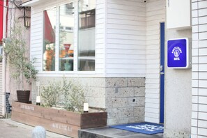 Edificio con una jardinera de madera con plantas, un felpudo azul en la entrada y un cartel que indica un albergue.