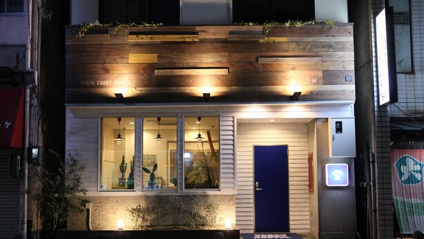 A modern hostel with a wooden facade, large windows, and a blue door. - North Front Hostel (Fukuchiyama)