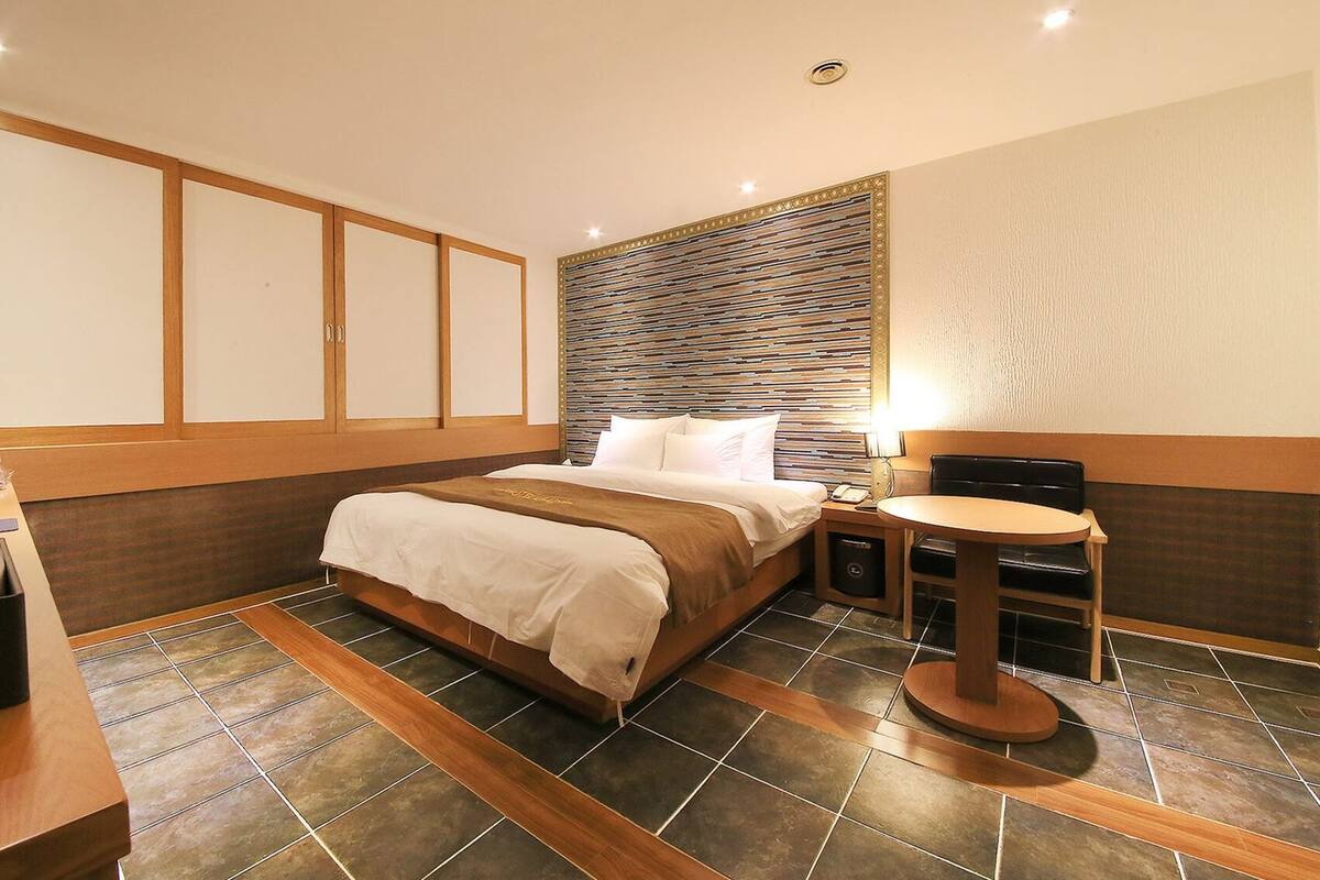 A hotel room with a bed, bedside table, and a small round table with a lamp.