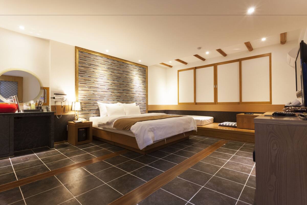 A modern bedroom with a large bed, a bedside table, a nightstand, a built-in wardrobe, and a large window.