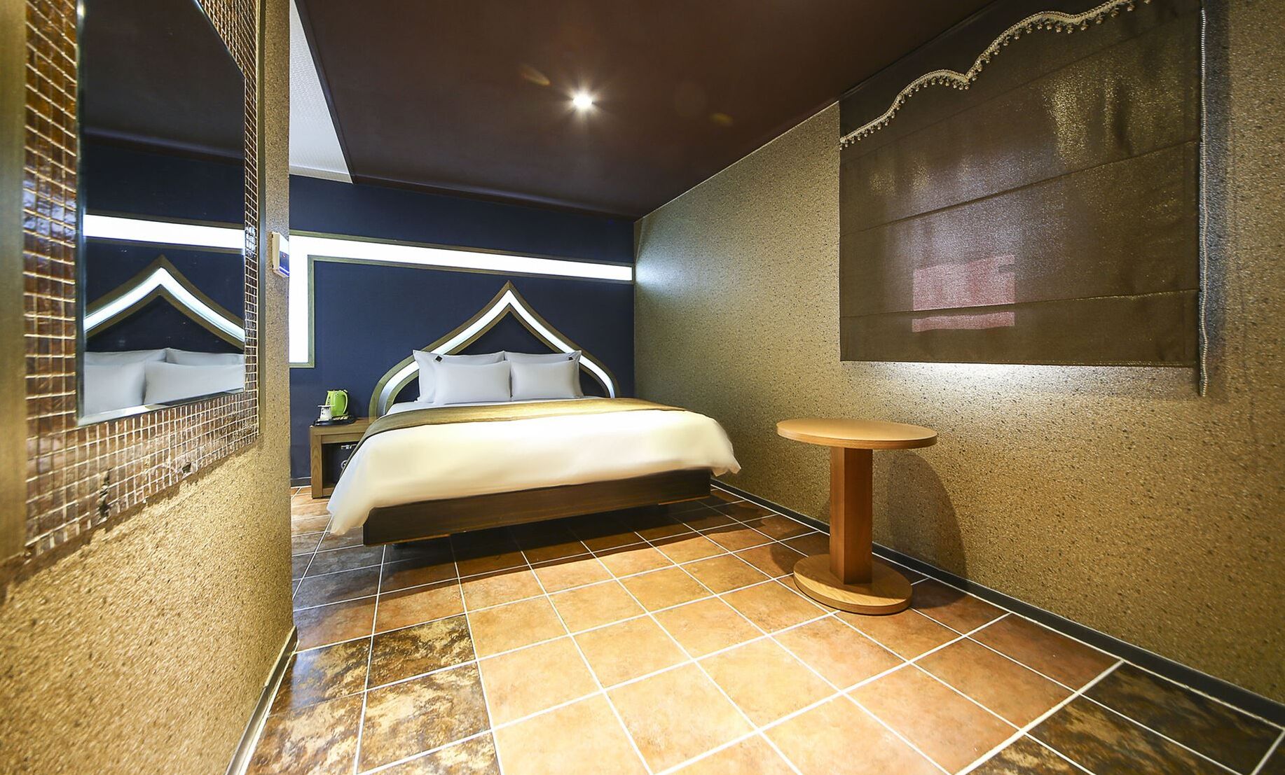 Une chambre à coucher avec un lit, une petite table ronde et une fenêtre donnant sur un immeuble.