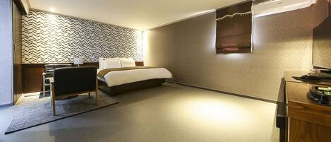 Habitación de hotel con cama, escritorio con silla, una mesita y aire acondicionado de pared.
