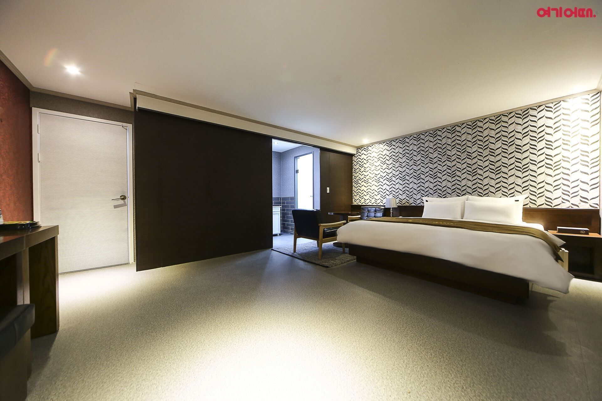 A modern hotel room with a large bed, a desk, and a wardrobe.