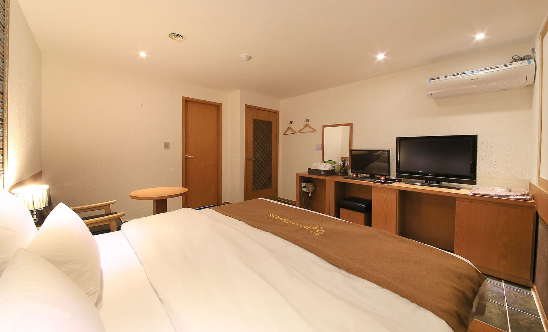 Habitación de hotel con cama, escritorio con computadora, televisor y aire acondicionado.