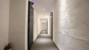 A long, narrow hotel corridor with a fire extinguisher on the left and a sign above the door on the right. - Hotel Leaders (Seoul)
