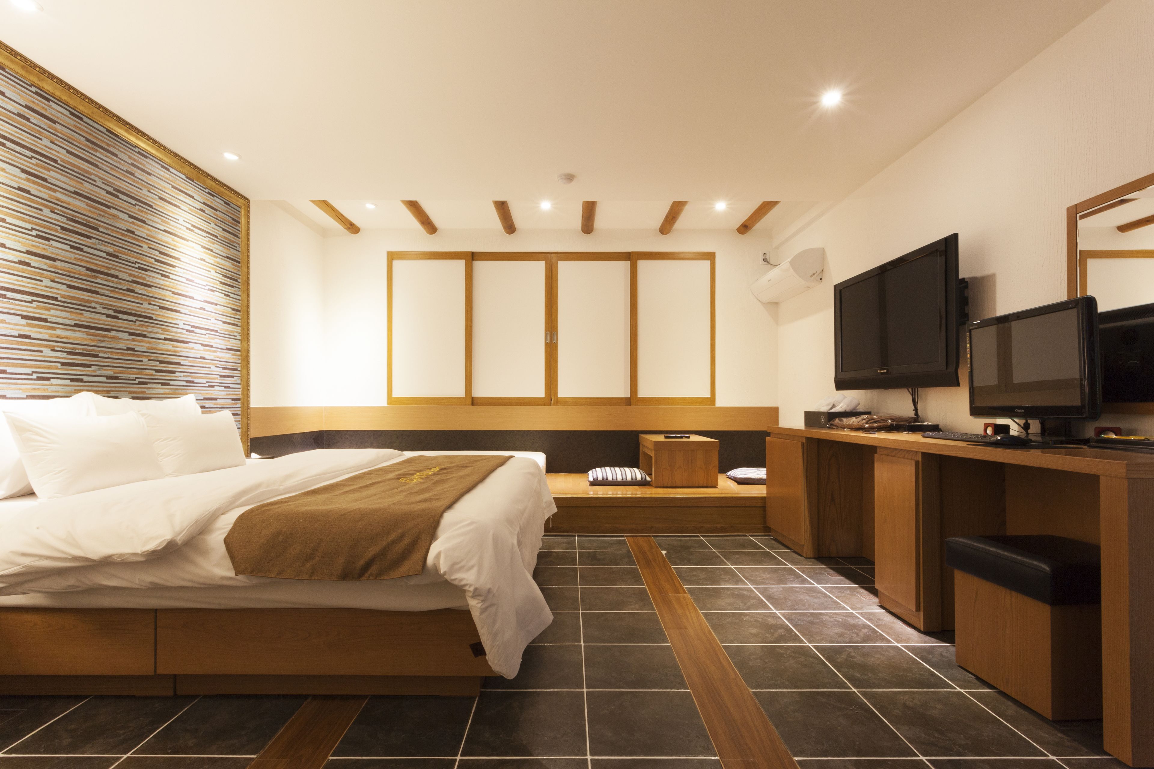 A modern hotel room with a large bed, a desk with a TV, and a seating area.
