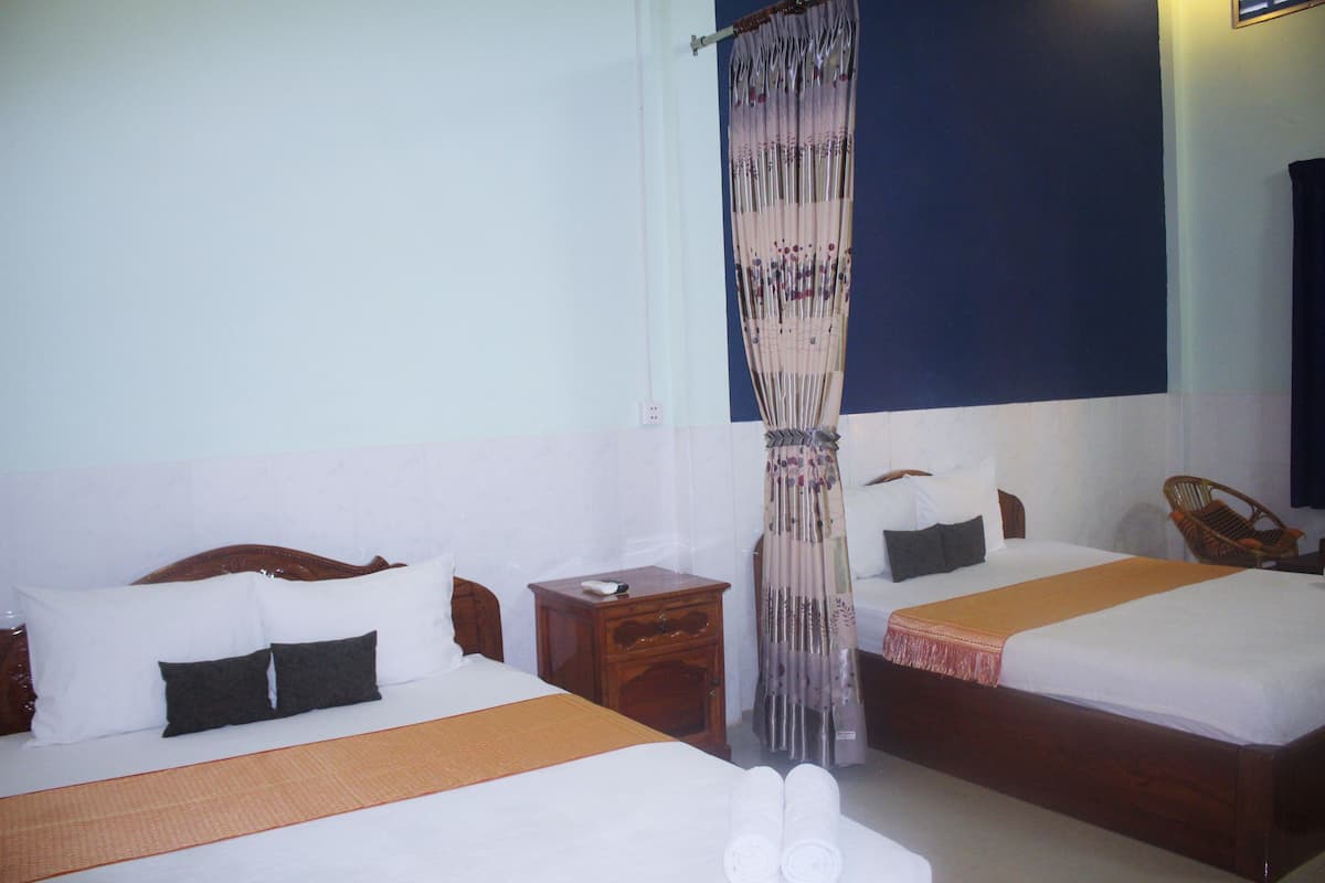 A hotel room with two beds, a wooden headboard, a nightstand, a chair, and a curtain.