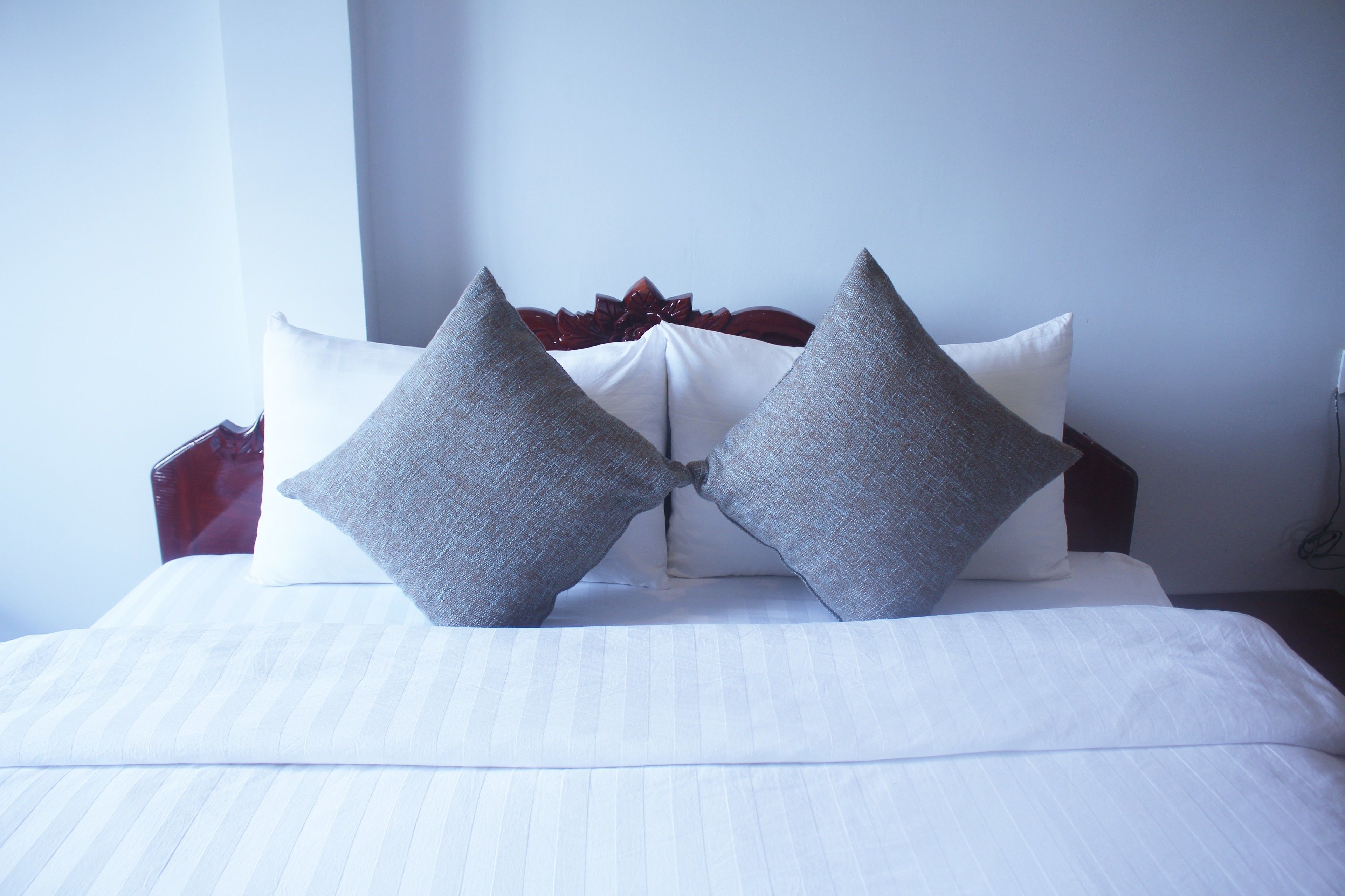 A neatly made bed with white linens and two gray pillows.