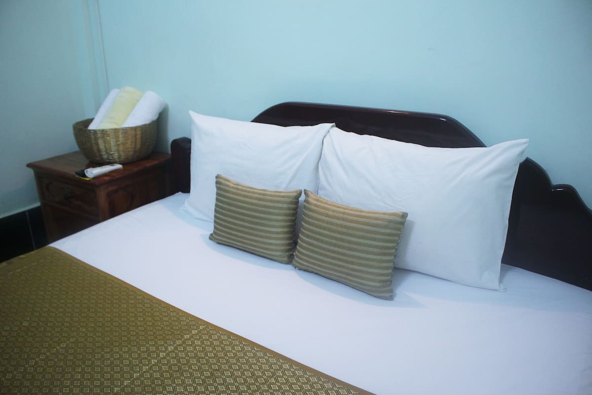 A neatly made bed with white and striped pillows, a wooden nightstand with a basket, and a remote control.