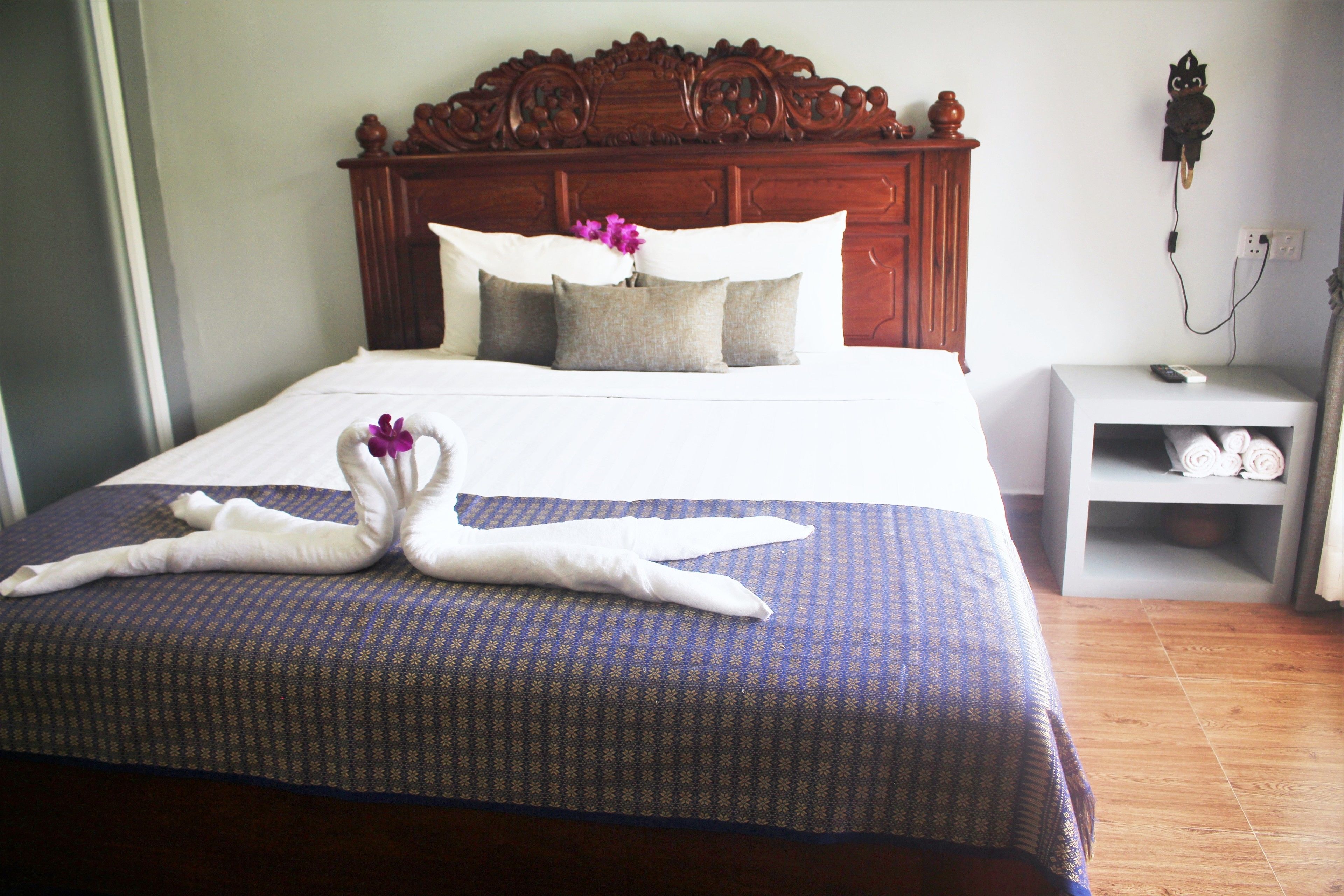 Una cama bien hecha con una colcha azul estampada y dos toallas con forma de cisne.