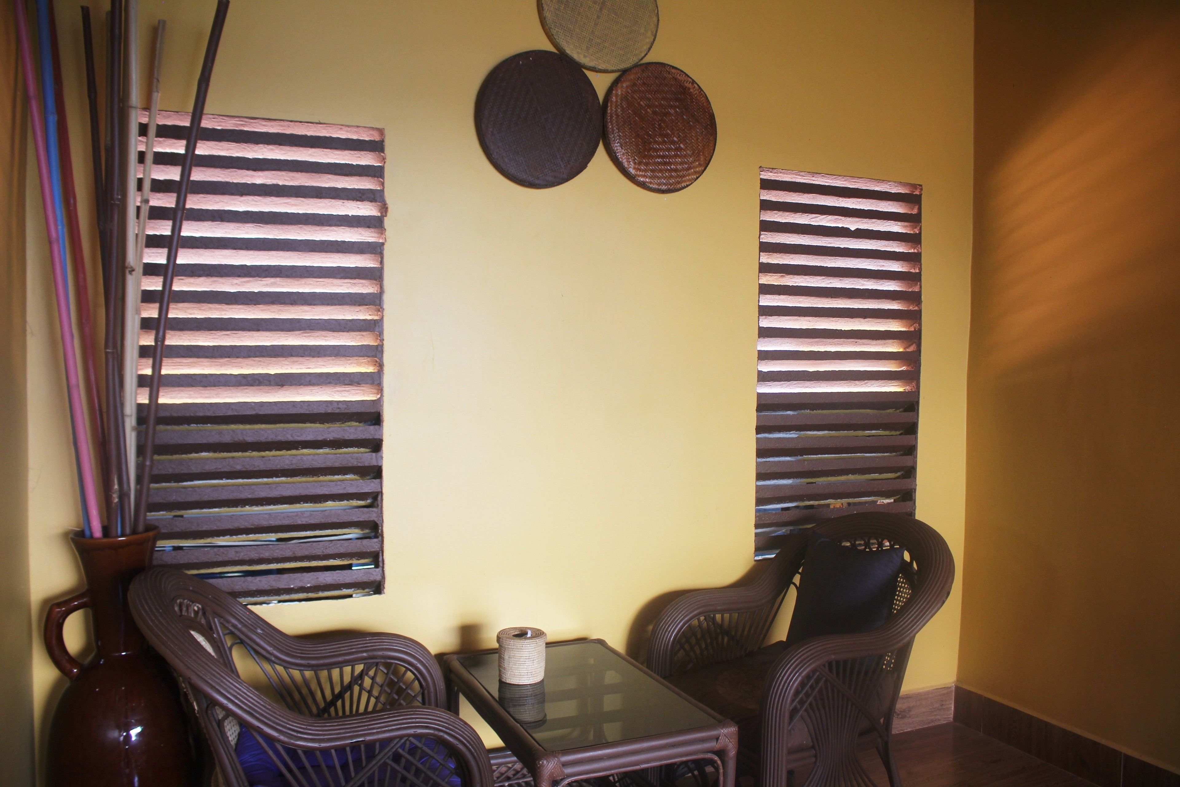 A room with two wicker chairs, a small table, and a vase with a rolled-up mat on it.