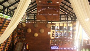 A rustic interior with a sign reading "Ramchang Guest House," wooden furniture, and traditional decor. - Ramchang Guesthouse (Battambang)