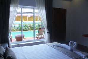 A hotel room with a large bed, a view of a swimming pool, and a chair by the window. - Ramchang Guesthouse (Battambang)