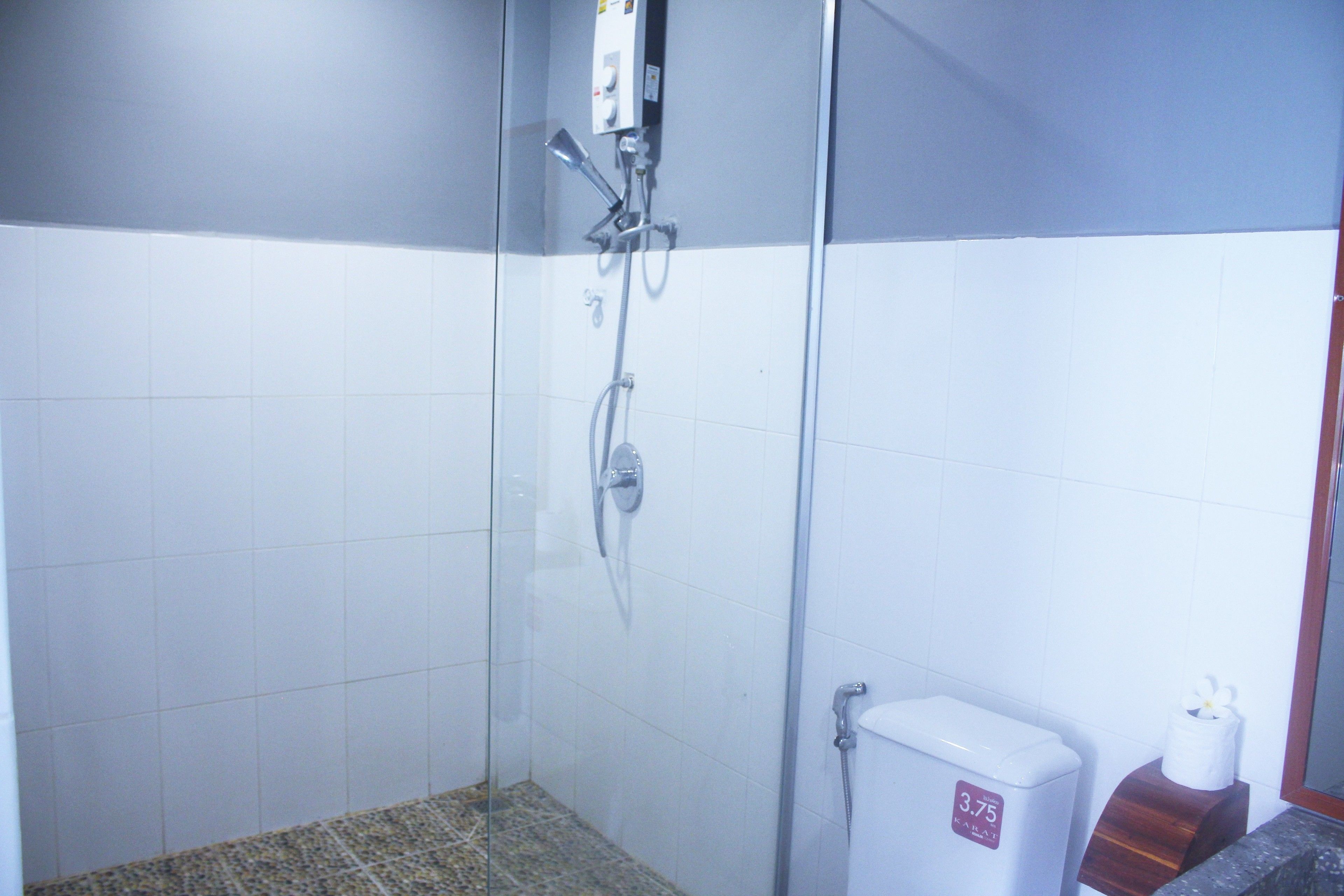 A bathroom with a glass-enclosed shower, a toilet with a price tag, and a wooden tissue holder.