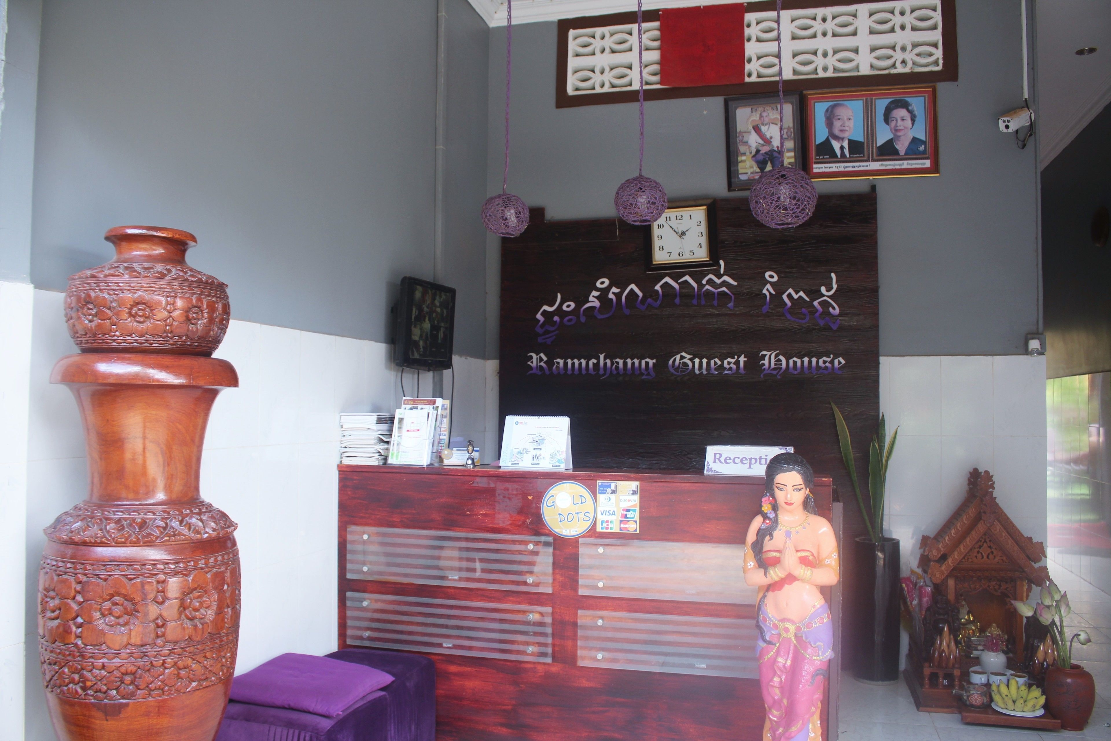 A reception desk with a sign reading "Ramchang Guest House," a large decorative vase, and a small shrine with offerings.