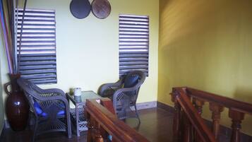 Um quarto com uma mesa de madeira, duas cadeiras de vime, um vaso grande e um corrimão de madeira.