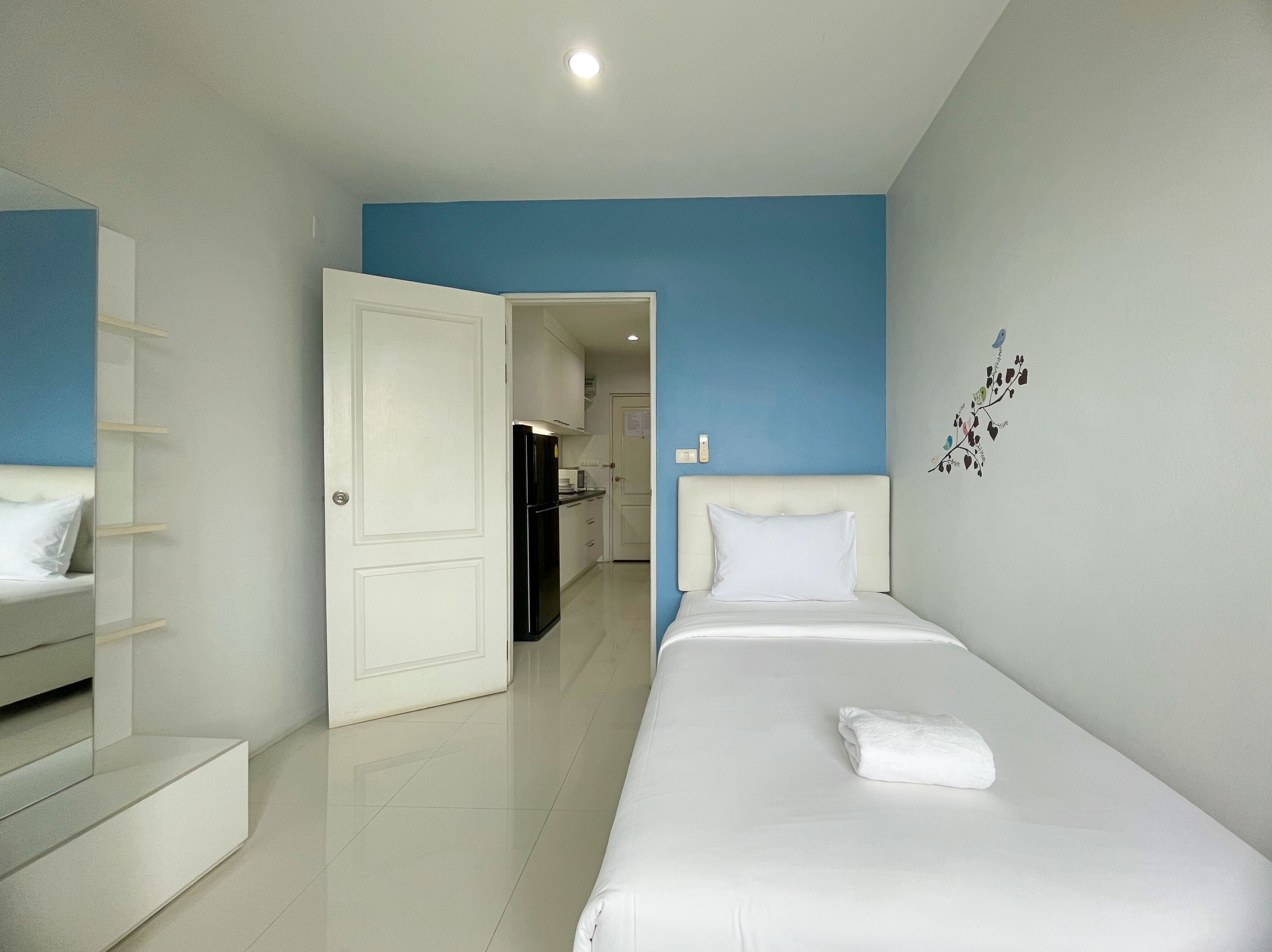A hotel room with a bed, a white wardrobe, a kitchen area, and a blue accent wall.