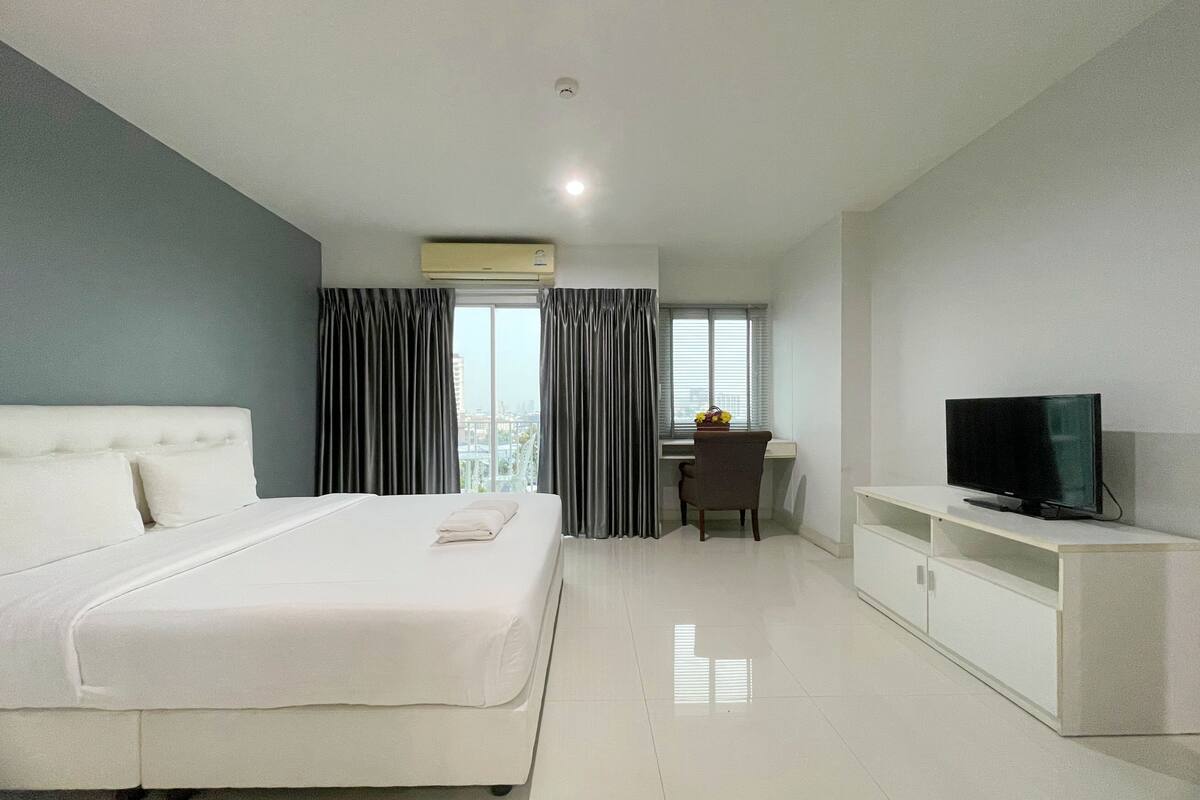 A hotel room with a bed, a desk, a chair, a television, and a window with curtains.