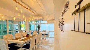 A dining area with white wicker chairs, a long table, and pendant lighting. - Baan Pattaya by Sabai (Pattaya)