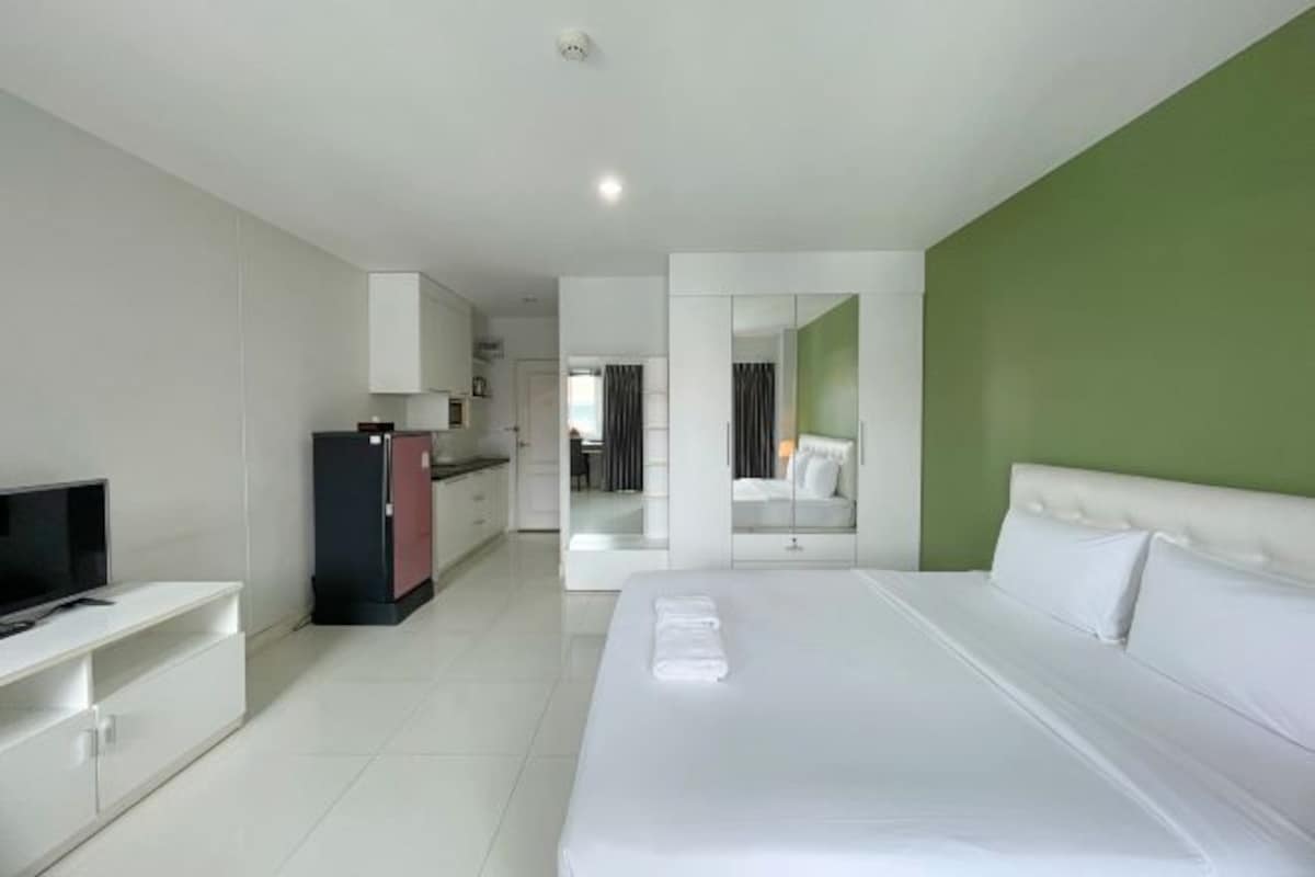 A modern hotel room with a large bed, a TV, a desk, and a wardrobe.