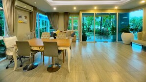 A spacious living area with a dining table, comfortable seating, and large glass doors leading to a garden. - Baan Pattaya by Sabai (Pattaya)