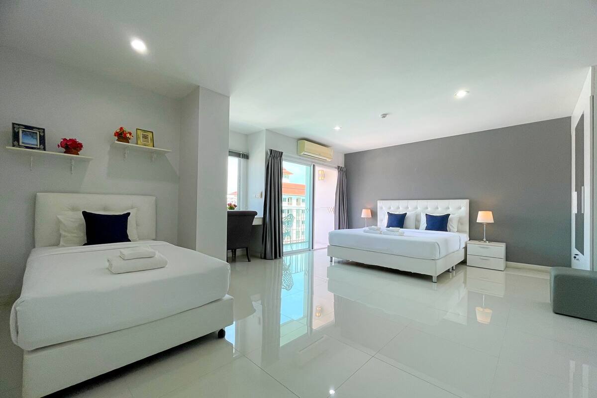 A modern hotel room with two beds, a desk, and a balcony with a view.