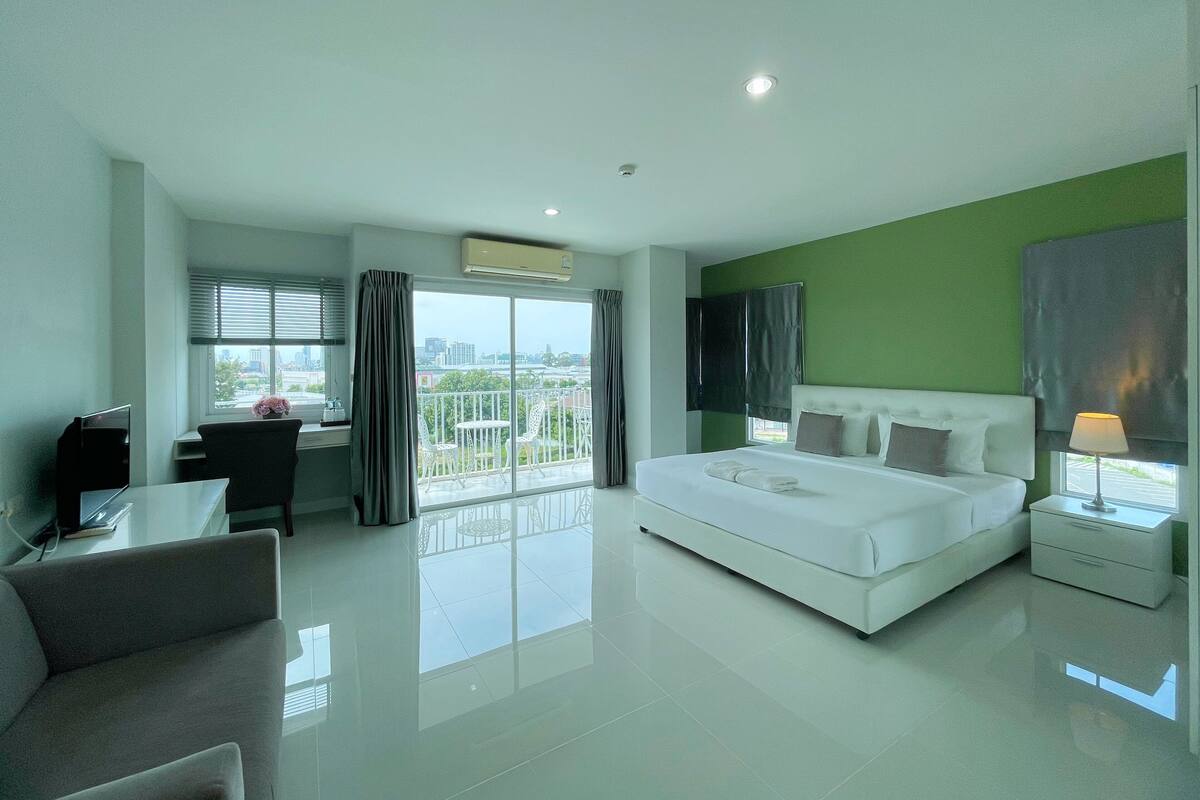 A modern hotel room with a large bed, a desk, and a balcony with a view.