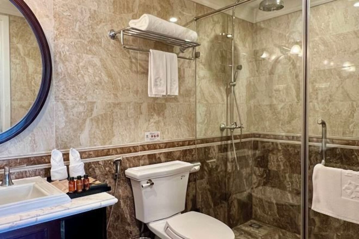 A bathroom with a marble wall, a glass shower enclosure, a toilet, a sink with a mirror, and a towel rack.