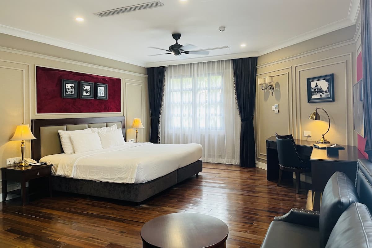 Habitación de hotel con una cama grande, un escritorio, una silla, un ventilador de techo y una ventana con cortinas.