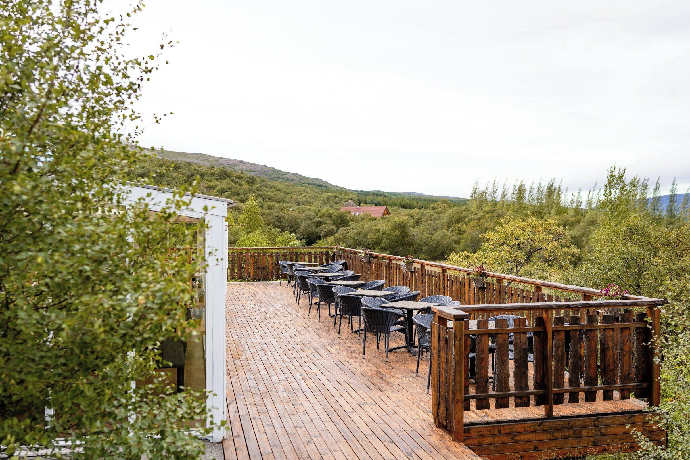 A wooden deck with outdoor seating, surrounded by greenery and hills.