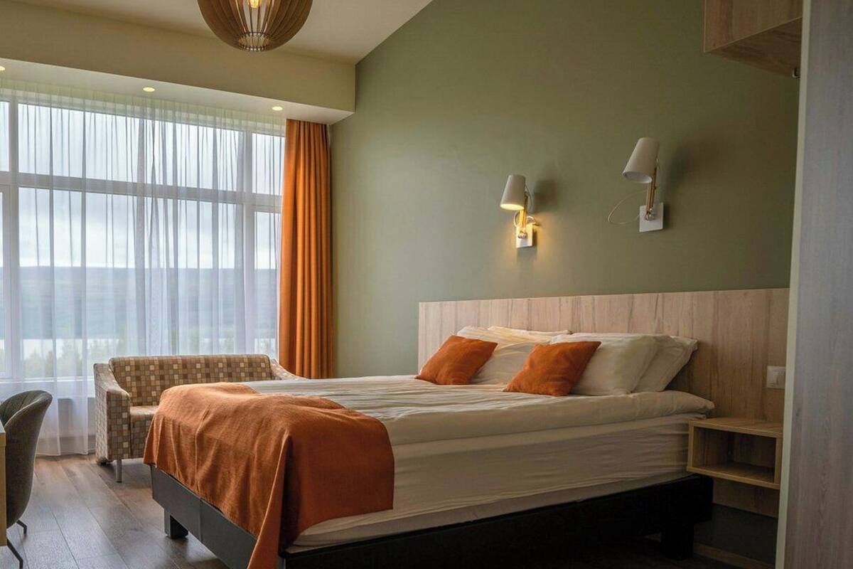 A hotel room with a bed, a chair, a desk, and a window with curtains.