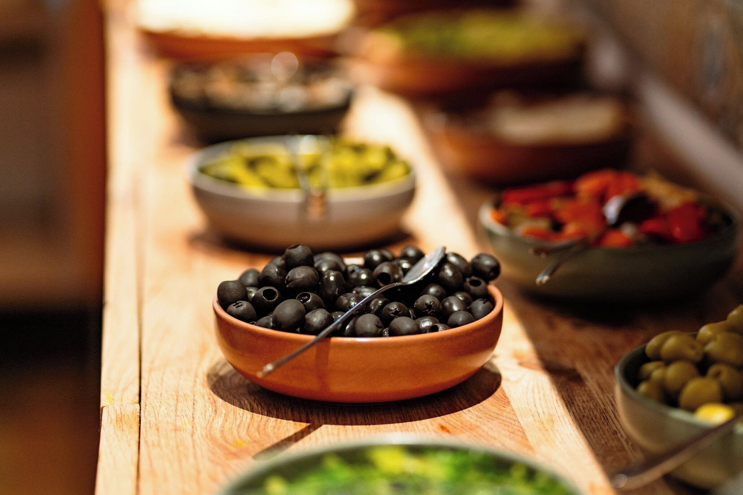 A wooden table with various bowls of olives and other food items.