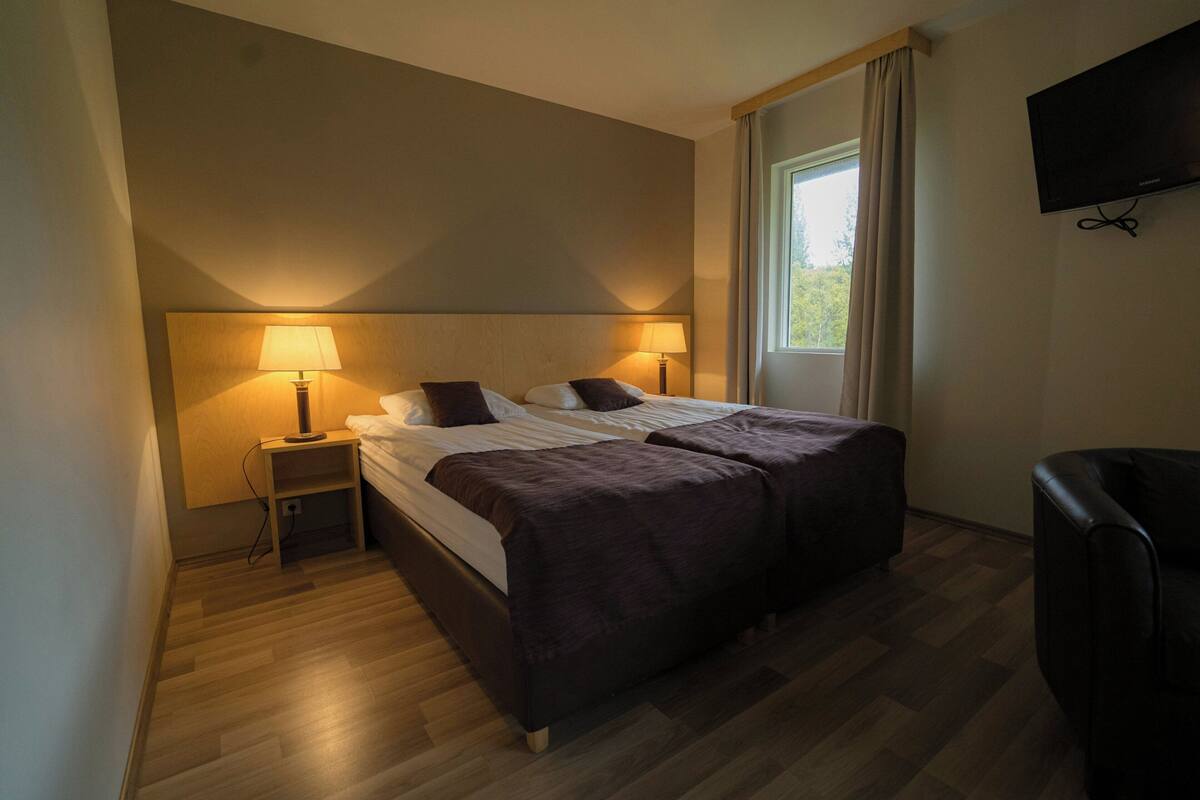 A hotel room with a bed, bedside lamps, a TV, and a window.