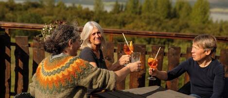 Three people seated at a wooden table outdoors with a scenic view in the background.