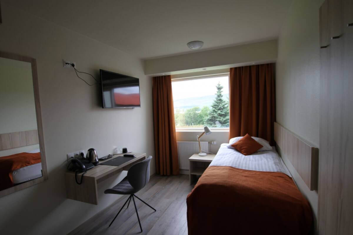 Ein Hotelzimmer mit Bett, Schreibtisch, Stuhl, Fernseher und einem Fenster mit Vorhängen.