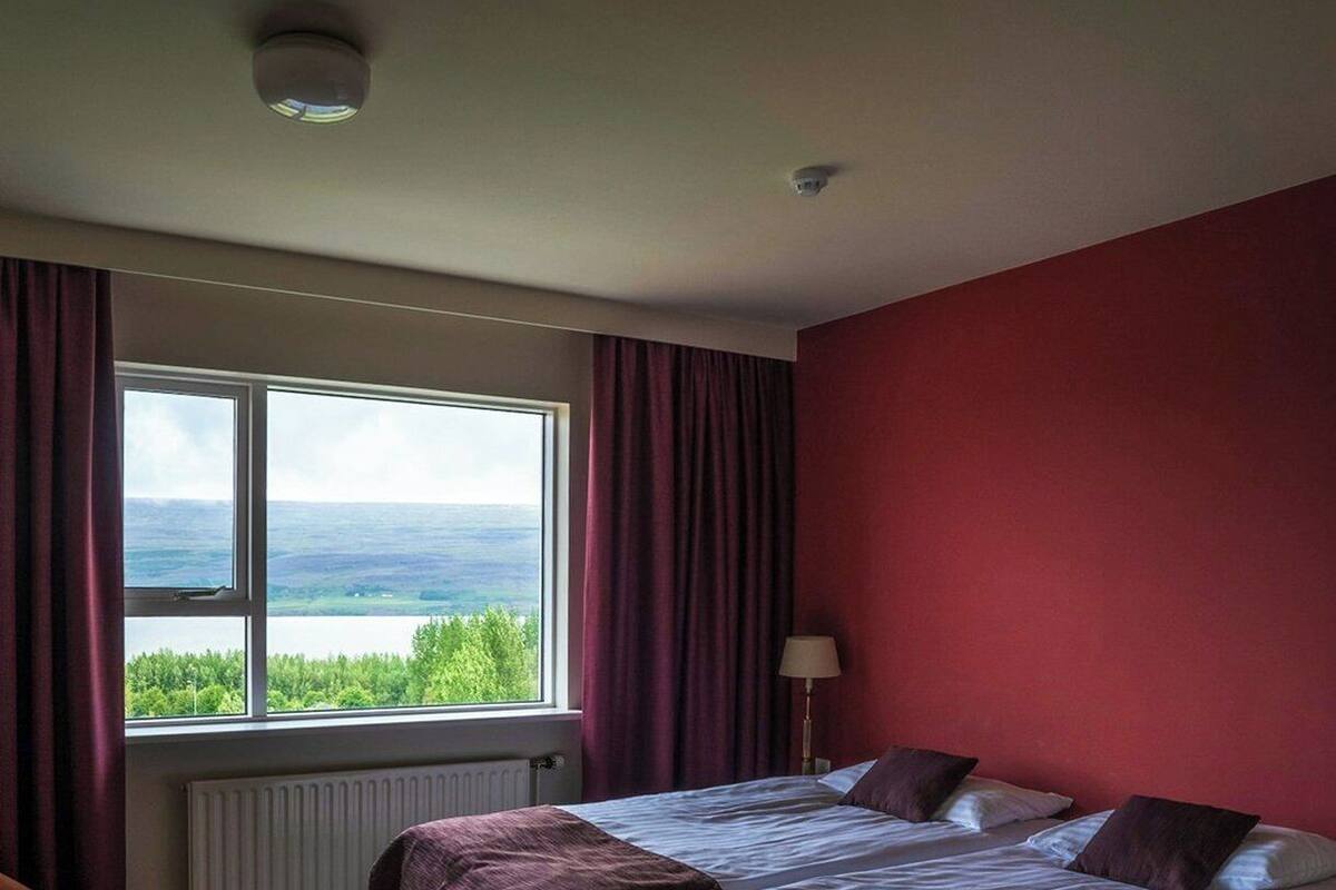 Ein Zimmer mit einem großen Bett, einem Fenster mit Blick, einem Heizkörper und einer Lampe.