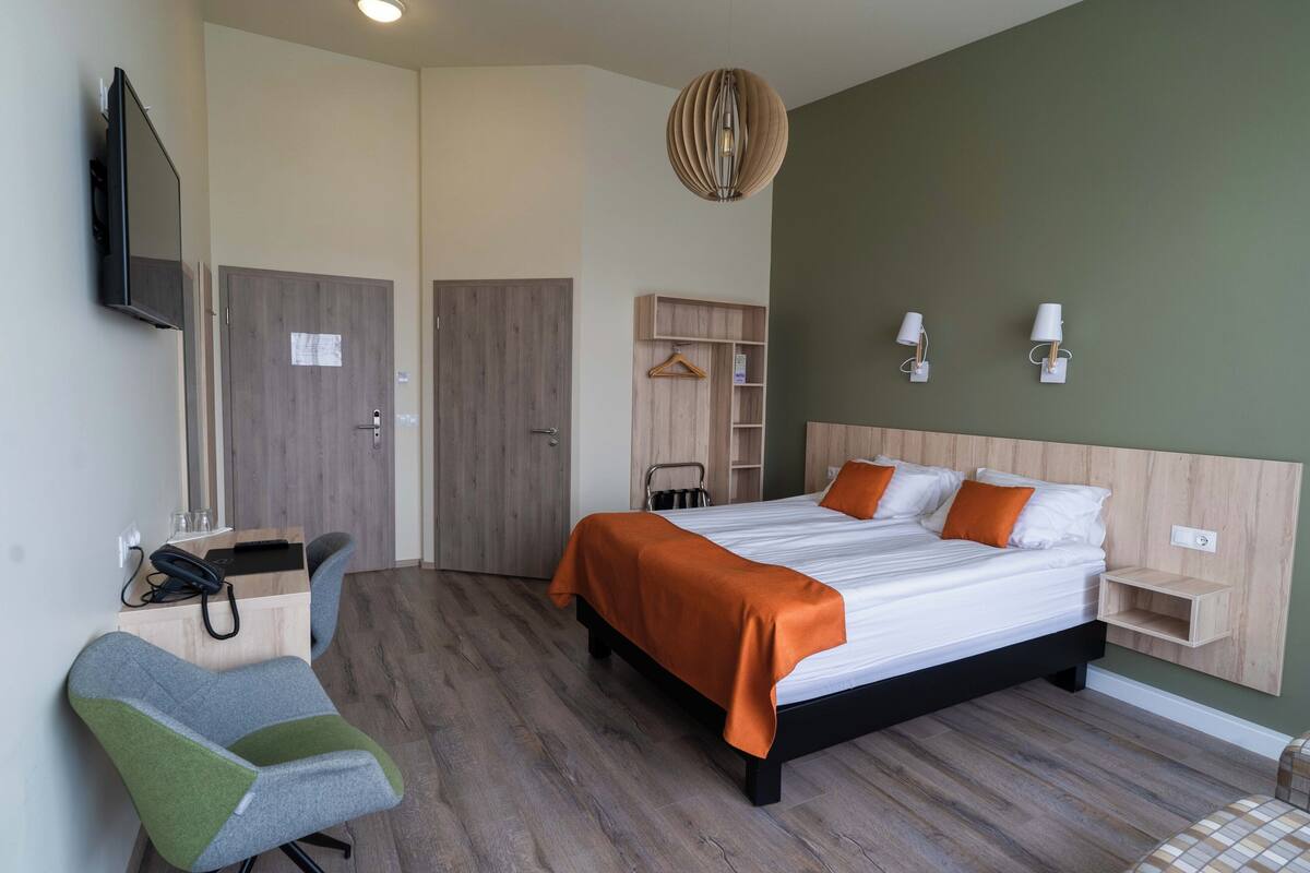 Ein modernes Hotelzimmer mit einem großen Bett, einem Schreibtisch mit Stuhl, einem Kleiderschrank und einem an der Wand befestigten Fernseher.