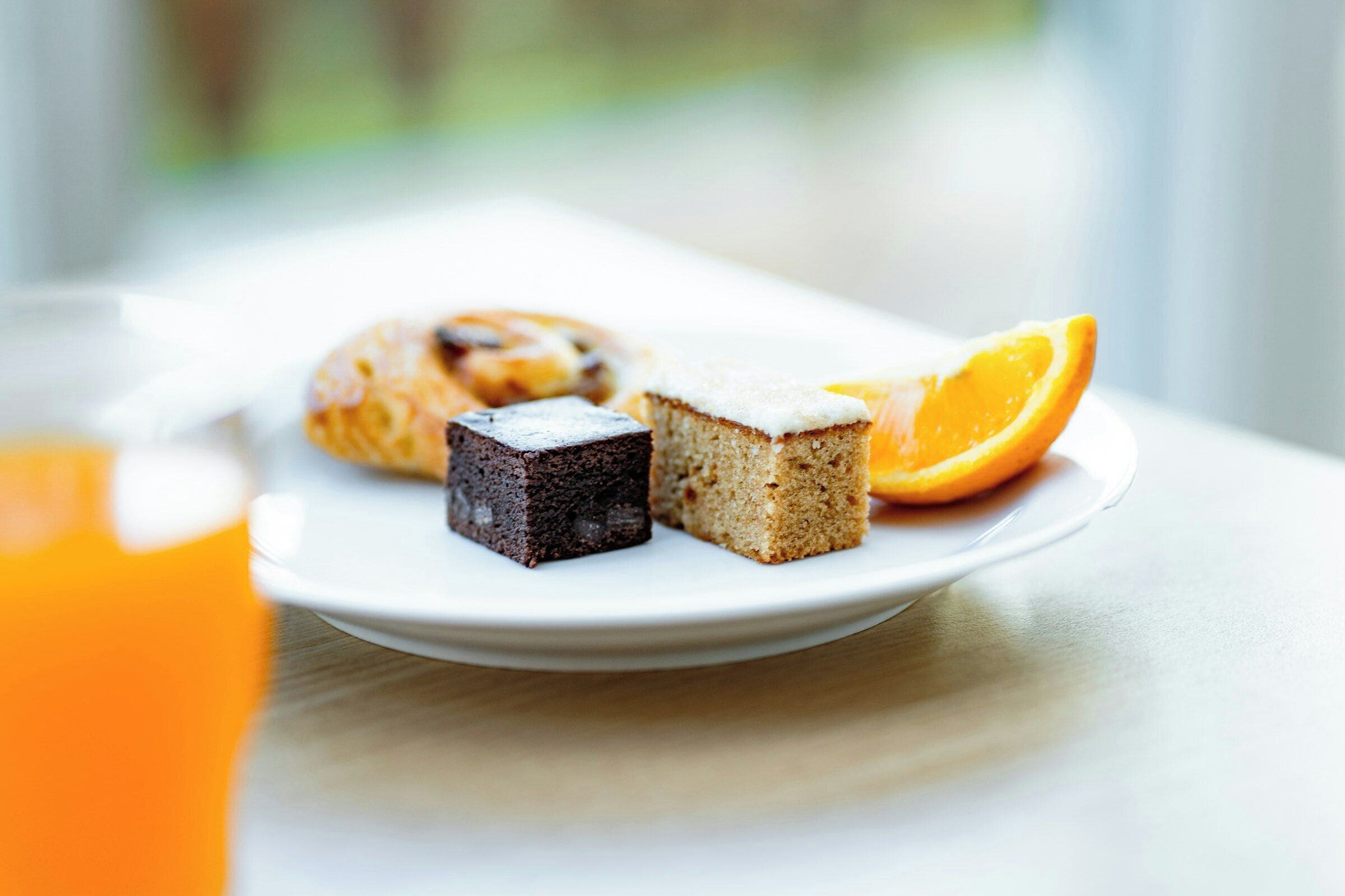 Une assiette contenant une part de gâteau, un muffin et une tranche d’orange, posée sur une table.