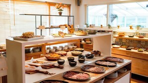 Buffet com diversos pratos e acompanhamentos, uma janela com persianas e uma estufa ao fundo.