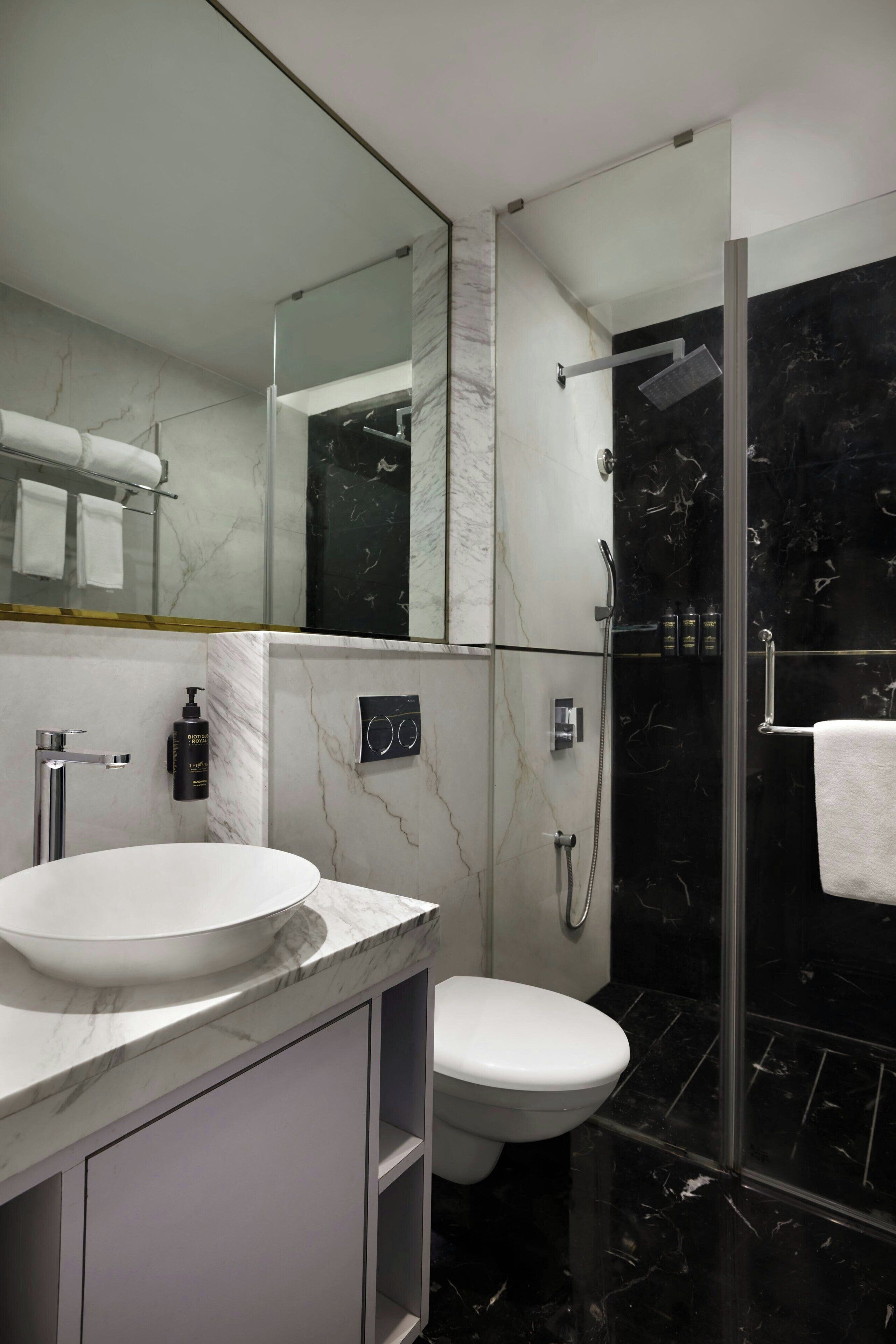 A modern bathroom with a marble sink, a toilet, a glass-enclosed shower, and a large mirror.