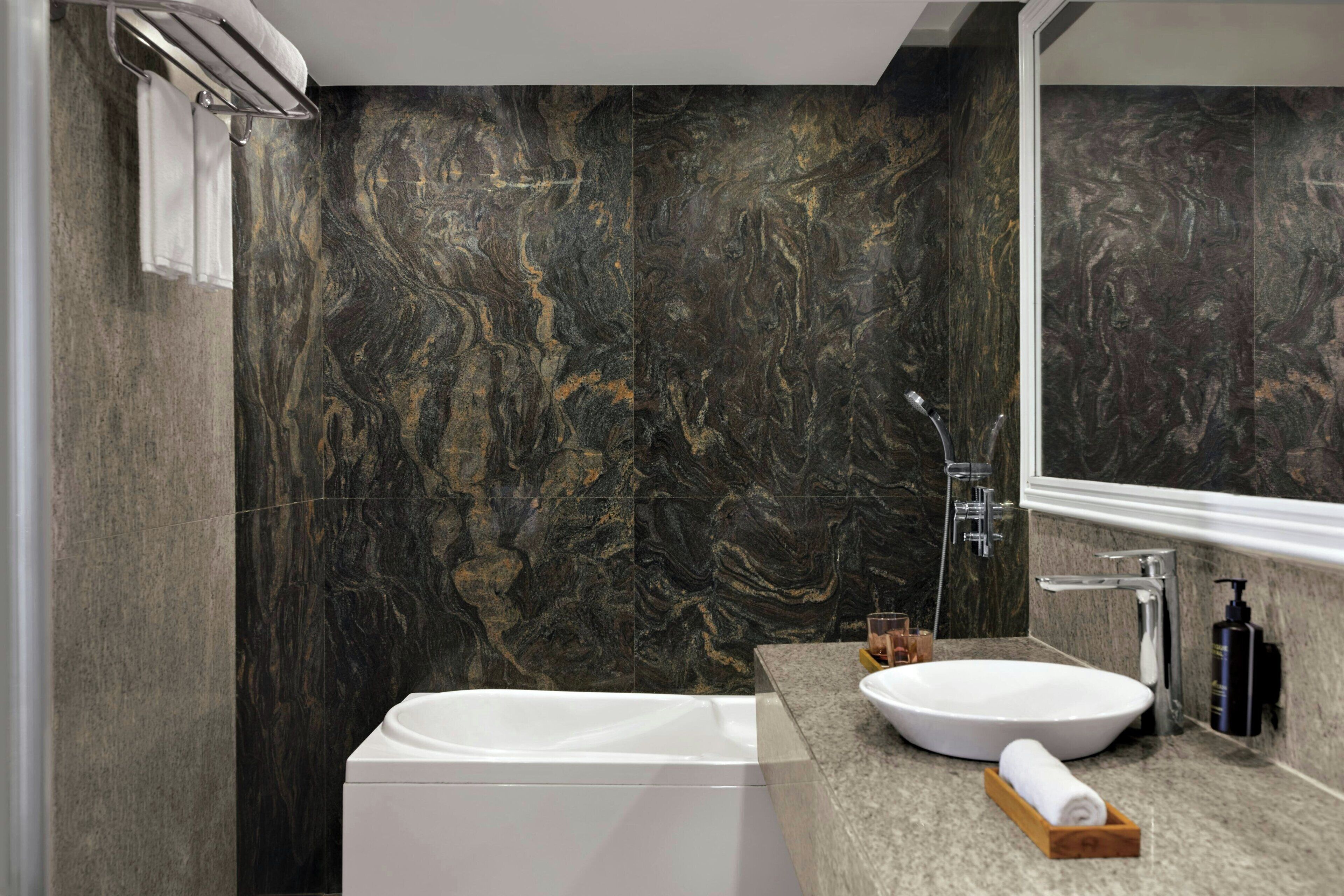 Un baño moderno con pared de mármol, una bañera blanca, un lavabo y un espejo.