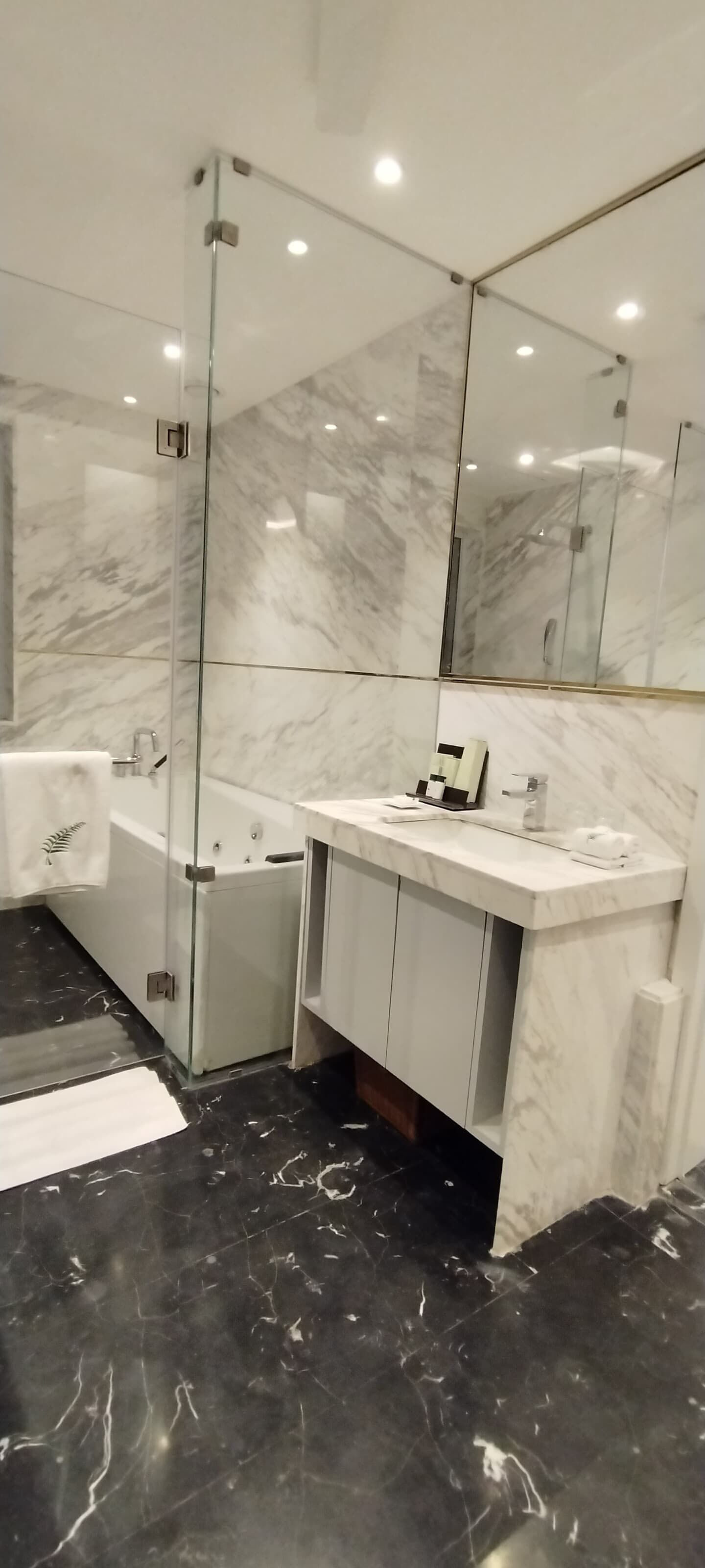 A modern bathroom with a glass-enclosed shower, a white marble bathtub, and a vanity with a mirror.