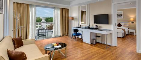 Una habitación de hotel moderna con sala de estar, mesa de comedor, kitchenette y balcón con vistas.